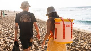 A couple walking on the beach, the woman is carrying the Yeti Hopper M20 backpack soft cooler