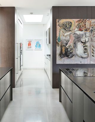 Modern kitchen with dark walls and kitchen island and white kitchen fixtures and flooring, with a large piece of modern art.