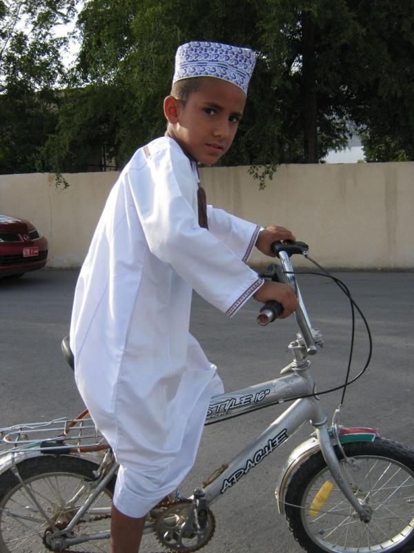 A young child rides in the more traditional Oman dress