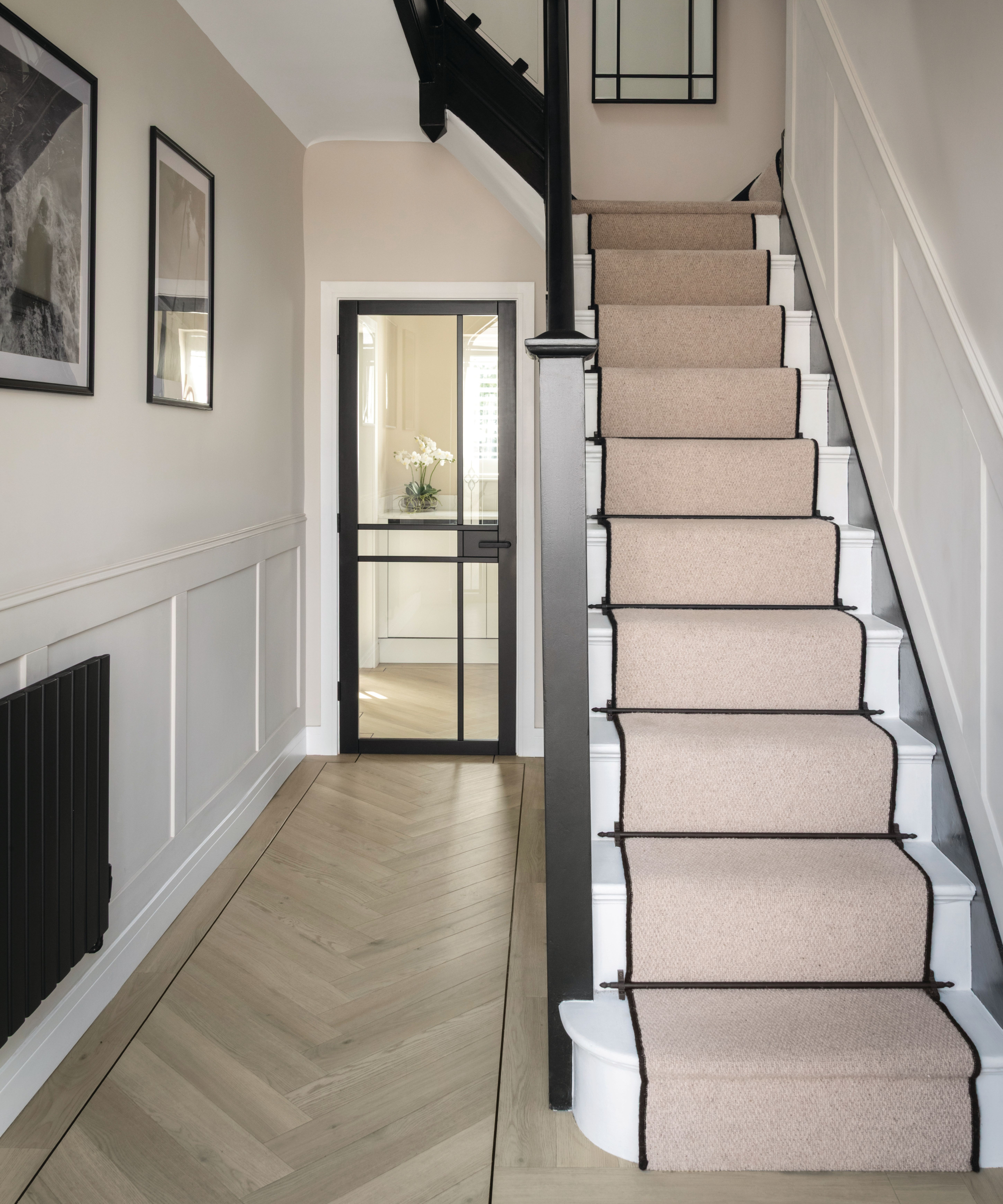 hallway with herringbone light wooden luxury vinyl flooring, beige carpet runner on white stairs, glass door at end of hallway
