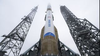 A blue and white rocket on the launch pad with towers on each side.