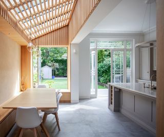 internal shot of kitchen extension with slatted ceiling to one side and white ceiling to other side, large kitchen island and dining table with built in bench seating area