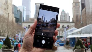 En person som håller upp en Samsung Galaxy S22 Ultra i en stadsmiljö med kameran aktiverad.