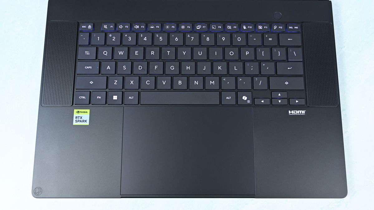 Top-down view of the keyboard deck showing flanking speaker grilles, power button, trackpad with DialPad icon, and RTX Spark sticker.