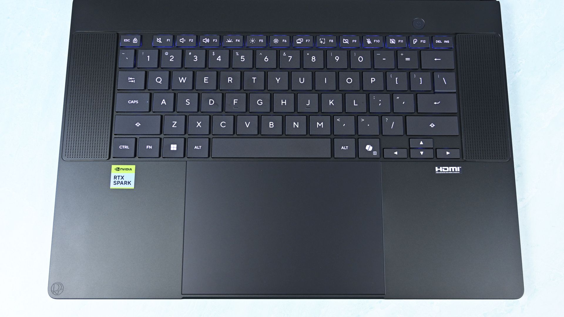 Top-down view of the keyboard deck showing flanking speaker grilles, power button, trackpad with DialPad icon, and RTX Spark sticker.