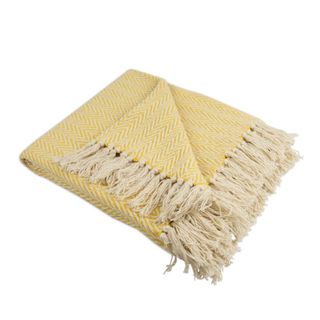 A folded marigold colored chevron patterned throw blanket with beige tassels and the corner folded at the top