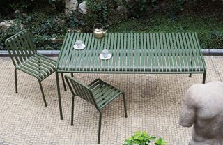 A green outdoor dining table and chairs on a paved patio