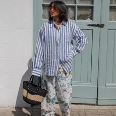 chiara wears white and blue striped button down and loose printed pants while holding a straw tote