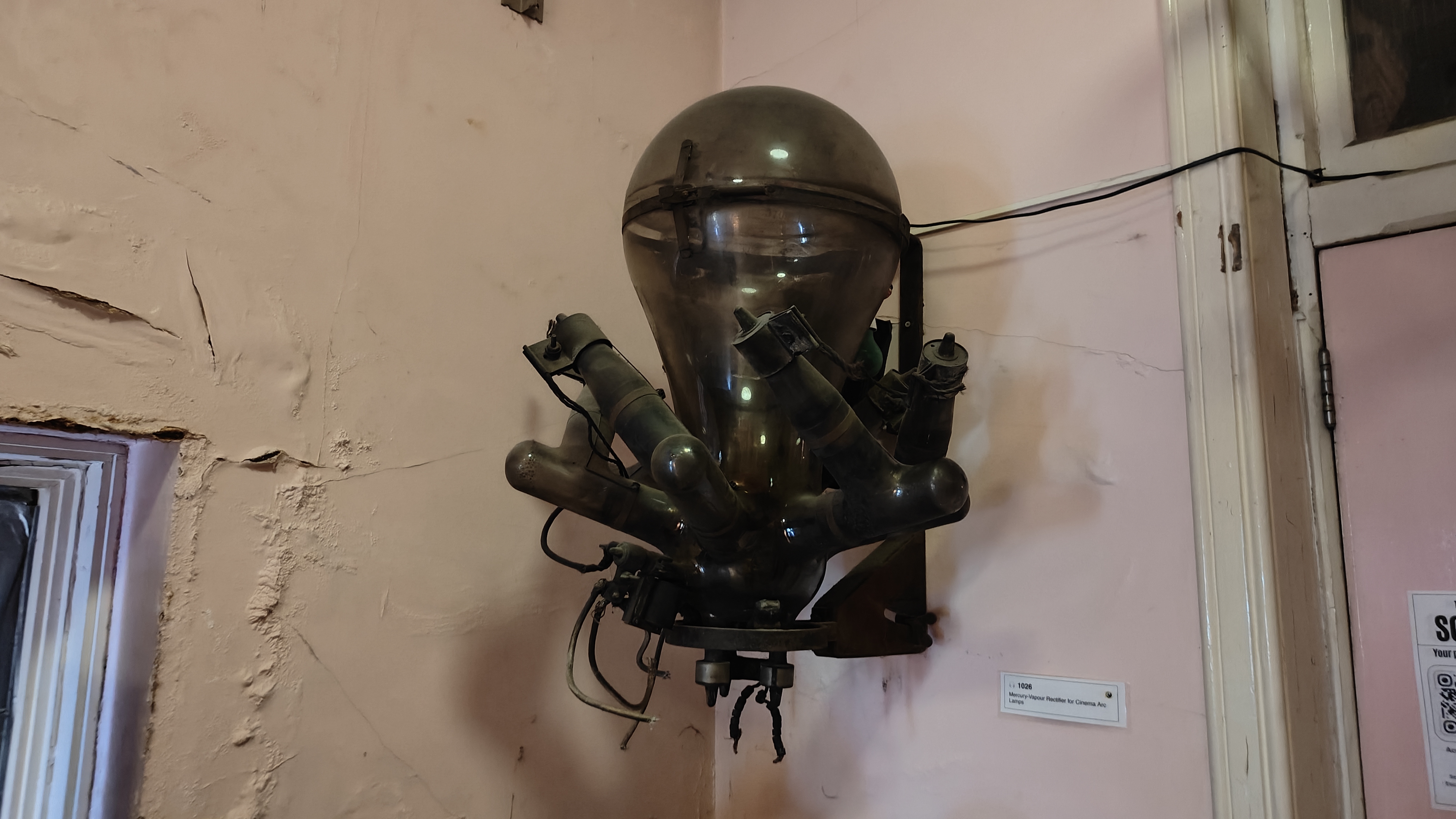 A mercury arc rectifier mounted on a white wall. It has eight arms and a big circular head.