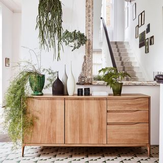 a hallway with a wooden sideboard below a large ornate mirror and plenty of greenery and plants