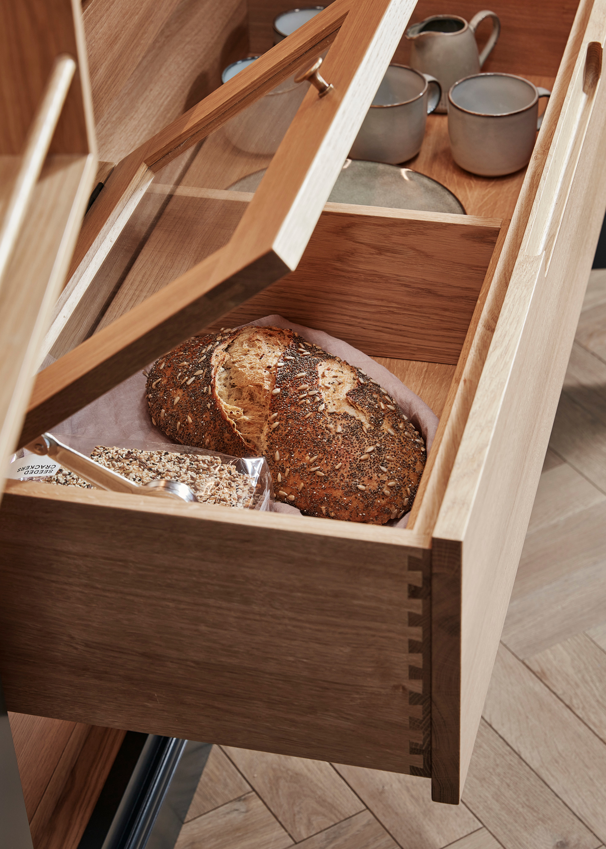 A close up of a wooden drawer with a bread storage box inside and glass lid on it