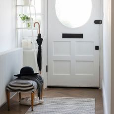 White hallway with a white wooden door and a storage rack and bench