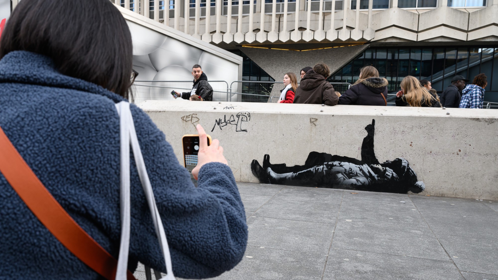A woman photographs a street artwork by Banksy in London. 