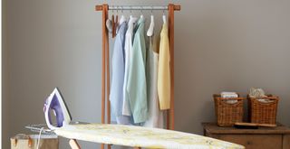 room with an ironing board and clothes rack with shirts hanging