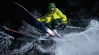 Young skier jumping of a cliff in a forest at night 