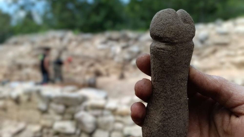 A person holding a stone carved into the shape of a penis. 