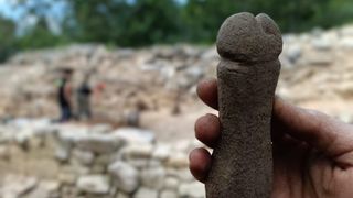 A person holding a stone carved into the shape of a penis. 