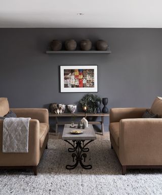 An example of dark living room ideas showing a living room with symmetrical brown leather seating in front of a grey wall