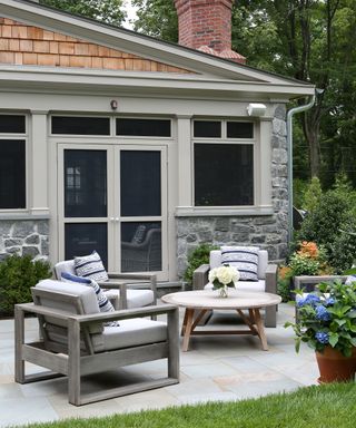 Small back yard landscaping ideas featuring a pale gray patio with gray wooden chairs around a circular coffee table, with potted hydrangeas.