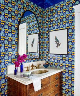 A powder room with dark blue and yellow wallpaper, and antique wooden vanity