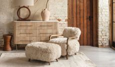 Sheepskin chair and foot rest with bare white brick wall and wooden drawers 
