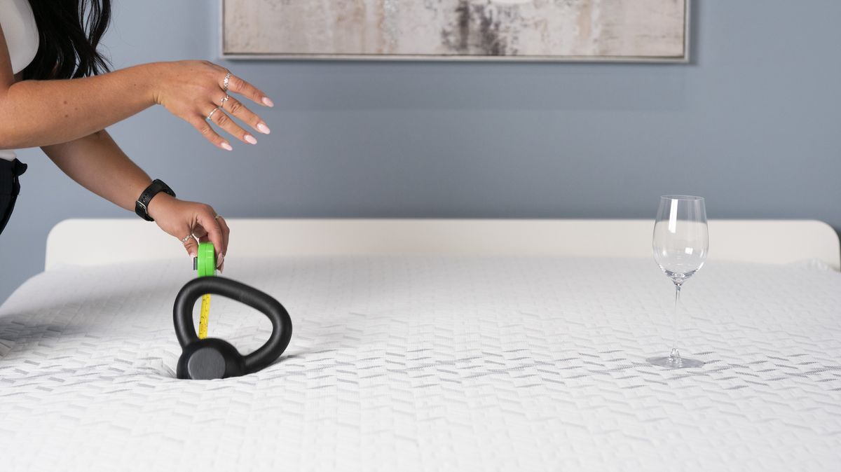 Image shows Tom's Guide Sleep Staff Writer Eve Davies conducting a motion isolation test on the Nectar Premier Memory Foam Mattress, using a weight and a wine glass to test how well this mattress isolates motion compared to the other beds in our best mattress guide