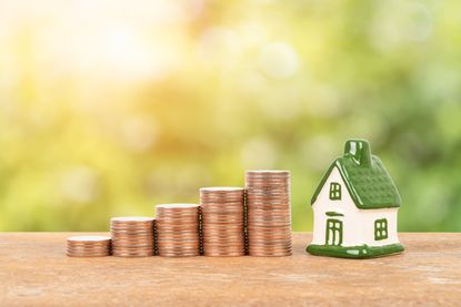Model house and coin stack on blurred green tree background