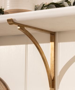 A gold metal bracket holding up a white shelf on a white wall