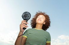 A woman is using a handheld fan on a sunny day