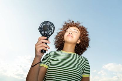 A woman is using a handheld fan on a sunny day