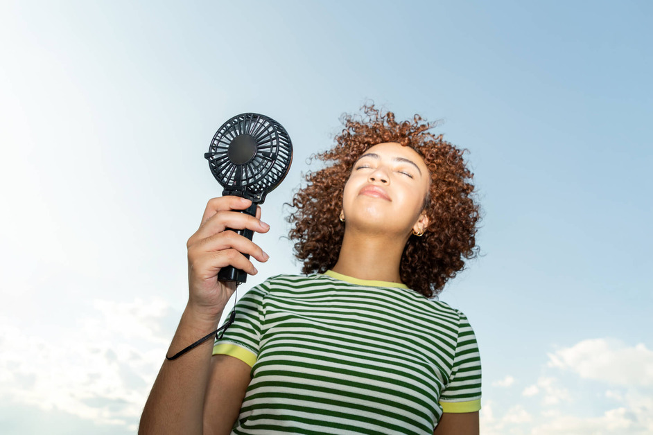 A woman is using a handheld fan on a sunny day