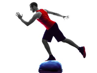 Man balancing on a balance trainer with one leg in a sprint start position