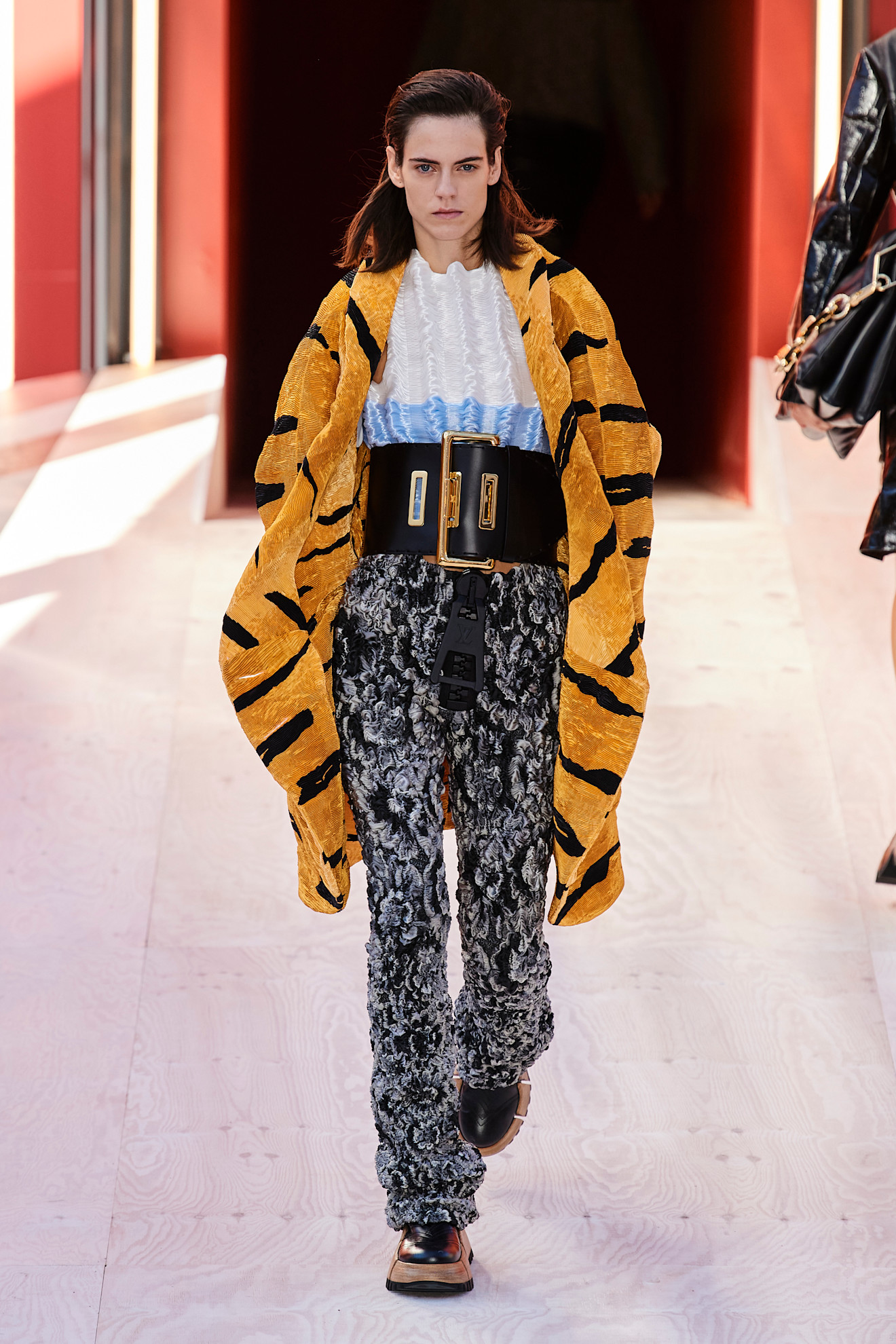 A model wearing an orange tiger print coat, white blouse, big black belt, and snakeskin pants at Louis Vuitton Spring 2023