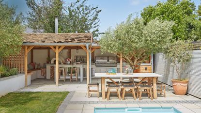 Mediterranean style outdoor kitchen with pool and wooden outdoor table 