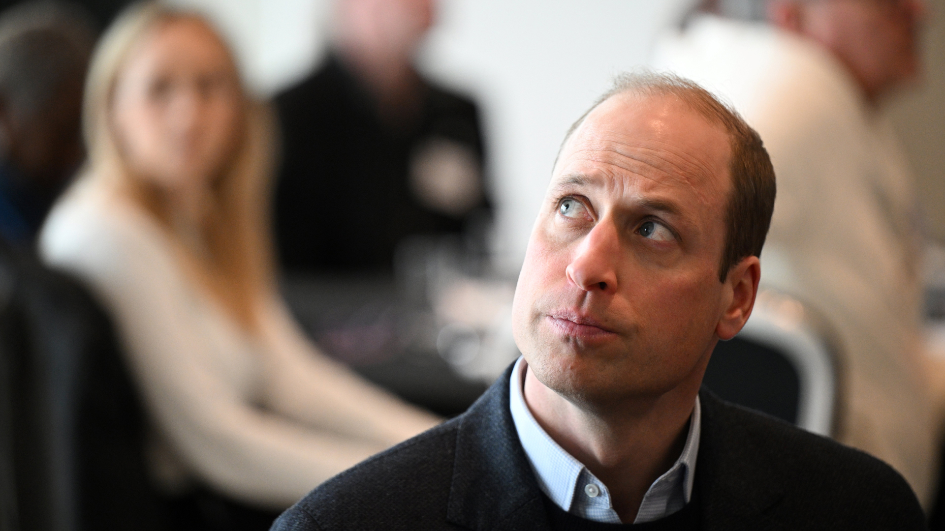 Prince William wears a shirt with a sweater and looks serious