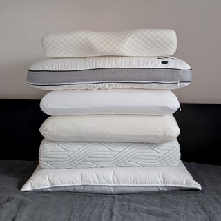 The best pillows for side sleepers being tested on a bed with a black headboard and grey bedding