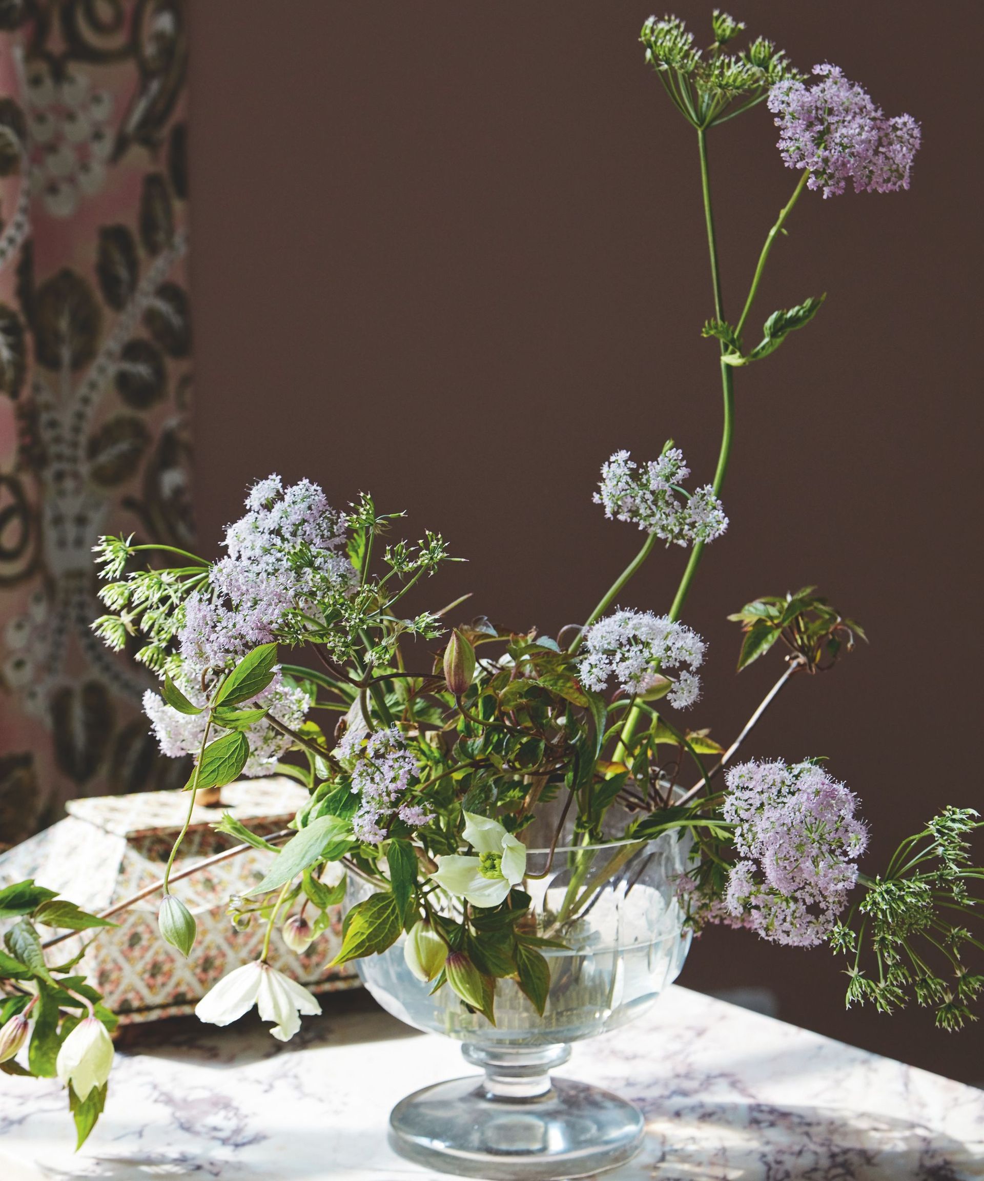 vase of soft purple and white flowers and greenery of varying heights in a low glass bowl vase