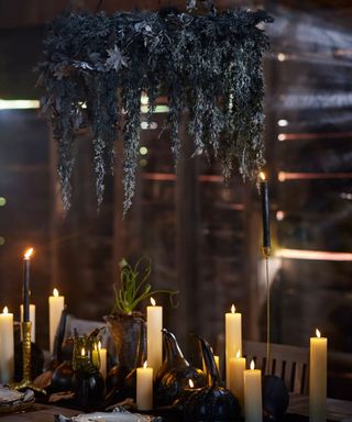 halloween table with centerpiece of candles and a large black foliage wreath suspended over the table