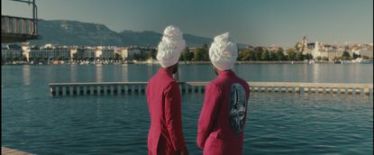 Two men in pink coats and white turbans look out over water