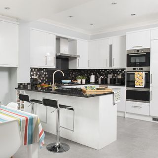 kitchen with white walls grey tiles with white cabinet and black granite platform