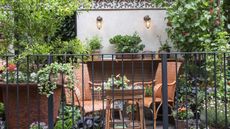 Two chairs and a table surrounded by shrubs and flowers in pots on a balcony at the RHS Chelsea Flower Show