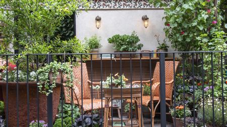 Two chairs and a table surrounded by shrubs and flowers in pots on a balcony at the RHS Chelsea Flower Show