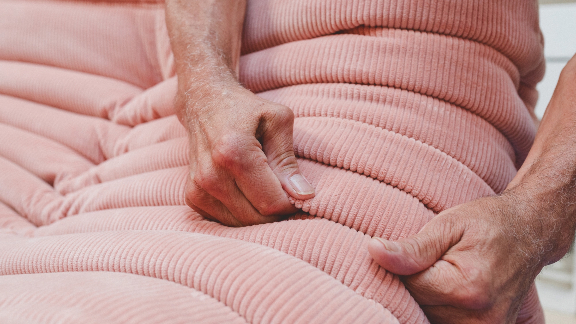 Close-up of a Ligne Roset upholsterer shaping and securing the soft pink folds of a Togo chair entirely by hand.
