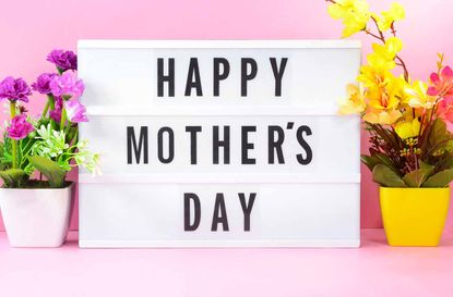 Happy Mothers Day text on light box with flowers on the background.