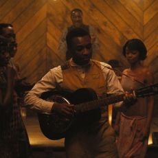 A man (Miles Caton as Sammie Moore) plays the guitar while standing in a crowd in a wooden barn, in 'Sinners.'