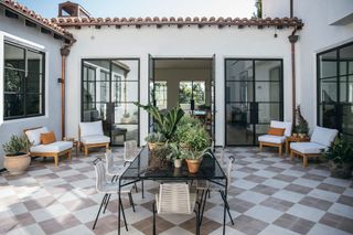 courtyard with checkered floor and dining table full of plants with white chairs around it and steel framed doors