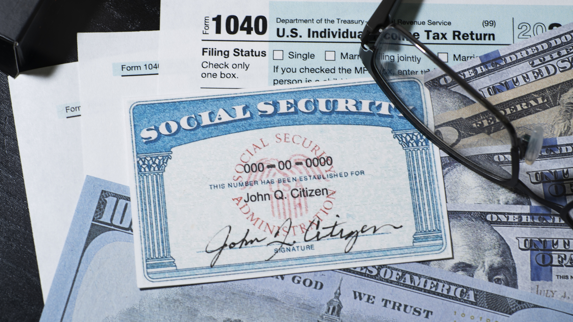 social security card with reading glasses on top of U.S. paper money and tax forms