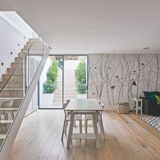 Basement room with staircase with sheet glass bannister, glass door to the garden, wooden flooring and large dining table with chairs