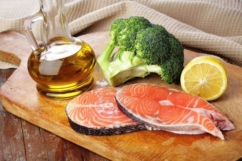 Salmon, olive oil, broccoli and lemon on a cutting board.