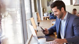 Eine Person benutzt ein Telefon und einen Laptop in einem Café.